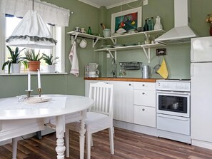 A kitchen with a white table, chairs, a stove, and shelves with various items.