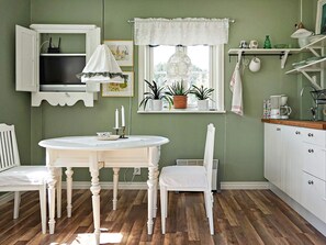 Une cuisine avec une table ronde, des chaises, une fenêtre ornée de plantes et un meuble blanc.