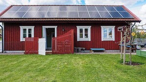 A red building with solar panels on the roof, a white door, and a fenced yard. - 2 Person Holiday Home in Rimforsa (Rimforsa)
