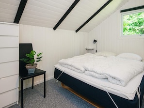 A bedroom with a bed, a small table with a plant, a wall-mounted lamp, and a window with a view of greenery. - 6 Person Holiday Home in Ansager (Ansager)