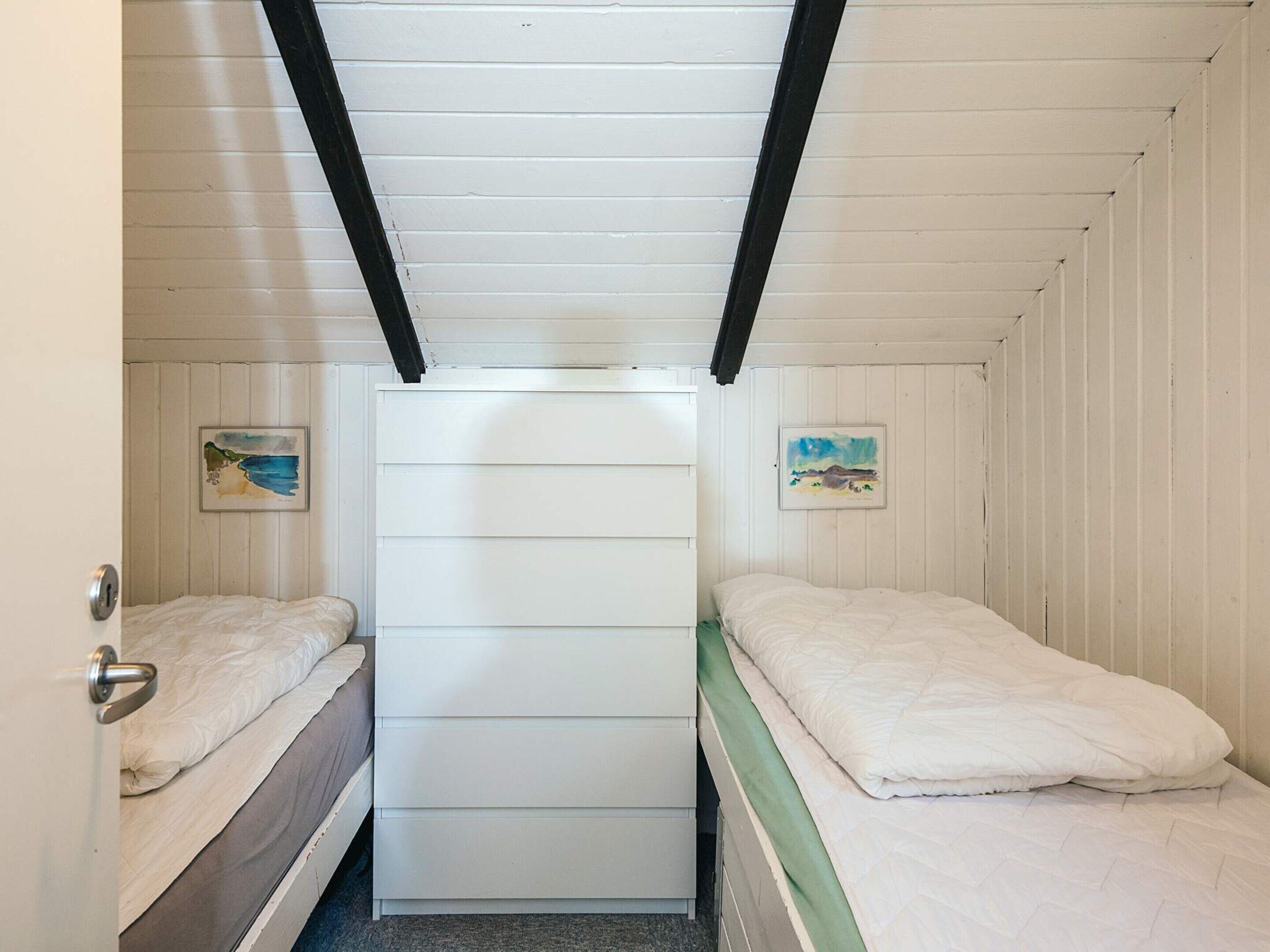 Un petit logement composé d’une seule pièce, comprenant deux lits, une armoire centrale et deux tableaux encadrés accrochés aux murs.