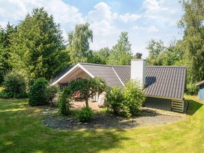 A single-story house with a sloped roof, surrounded by a well-maintained lawn and dense trees. - 6 Person Holiday Home in Ansager (Ansager)