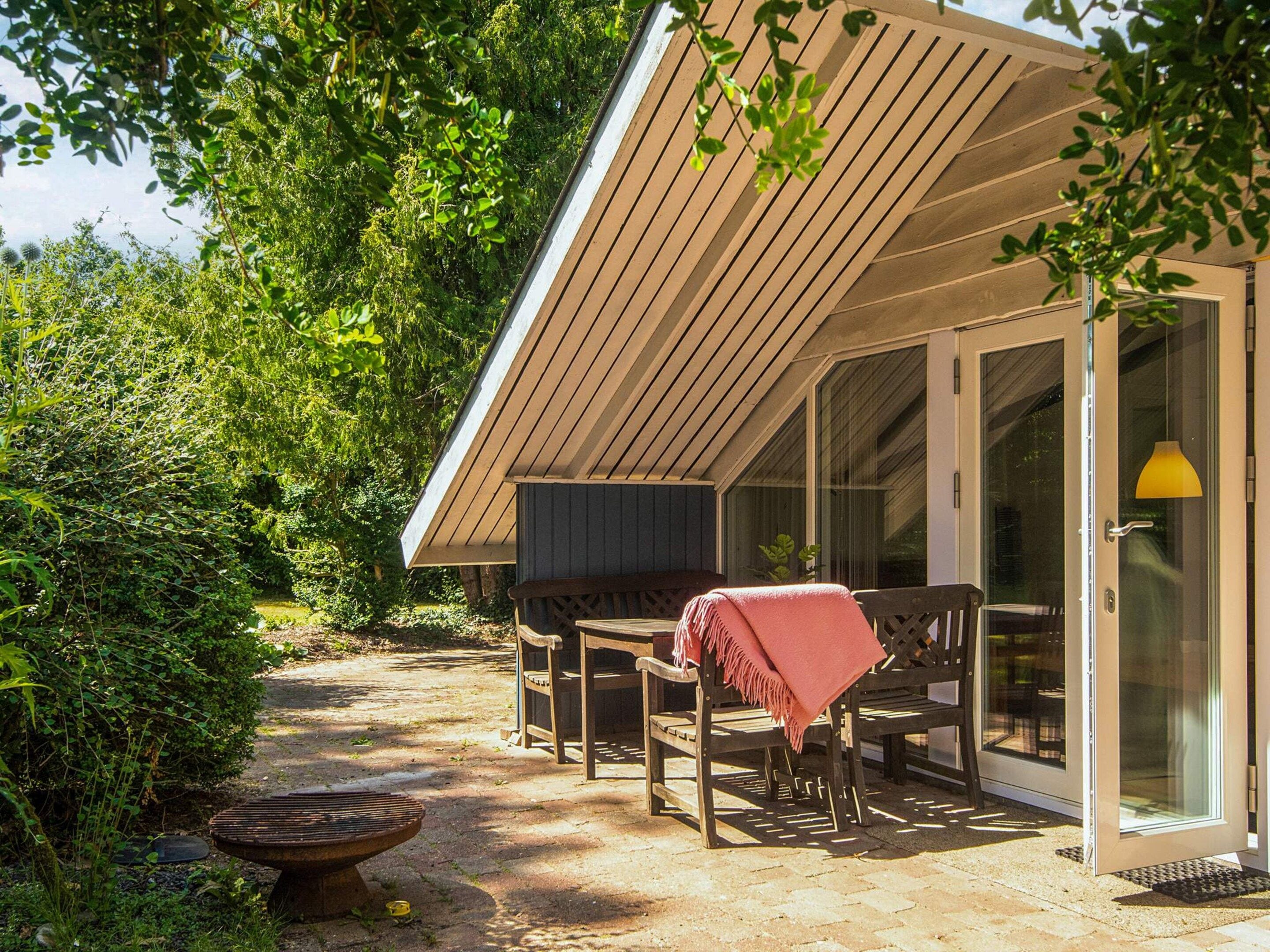 A covered outdoor seating area with a bench and a table, a door with a glass panel, and a fire pit.