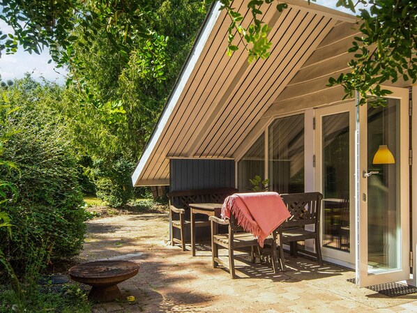 A covered outdoor seating area with a bench and a table, a door with a glass panel, and a fire pit.