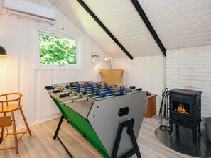 Une pièce avec une table de baby-foot, une cheminée et une fenêtre donnant sur un paysage verdoyant.