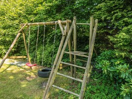 Un columpio de madera con un neumático colgante y una escalera en un jardín.