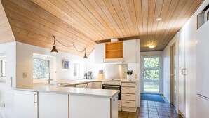 A modern kitchen with white cabinetry, a central island, and a wooden ceiling. - 10 Person Holiday Home in Norre Nebel (Norre Nebel)