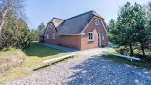 A two-story brick house with a sloped roof, a gravel driveway, and a bench in the foreground. - 10 Person Holiday Home in Norre Nebel (Norre Nebel)