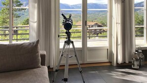 Ein Teleskop auf einem Stativ in einem Raum mit großen Fenstern mit Blick auf eine Berglandschaft.