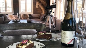 Ein Esstisch mit einer Champagnerflasche, zwei Tellern mit Kuchenstücken und einem Stativ in einem gemütlichen Wohnzimmer mit einer Couch und einem Fenster.