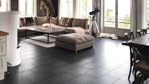 Ein modernes Wohnzimmer mit einem Ecksofa, einem Couchtisch und einem Esstisch mit Stühlen. Ein Stativ mit einer Kamera steht daneben, und ein Hund liegt auf dem Boden.