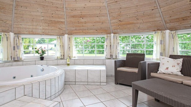 Un área de spa con jacuzzi, mobiliario de mimbre y amplios ventanales con cortinas.
