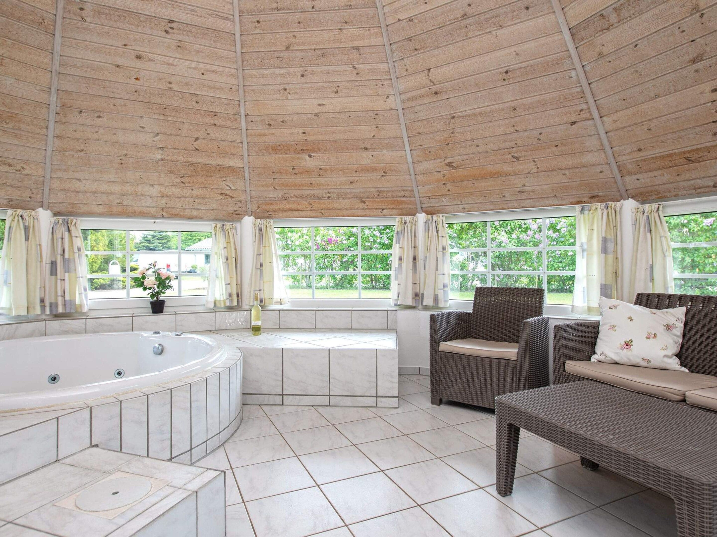 A spa area with a hot tub, wicker furniture, and large windows.