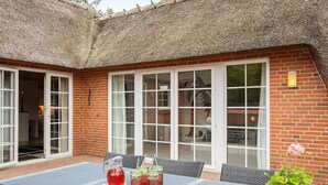 Un patio con una mesa lista para comer, techo de paja y pared de ladrillo.