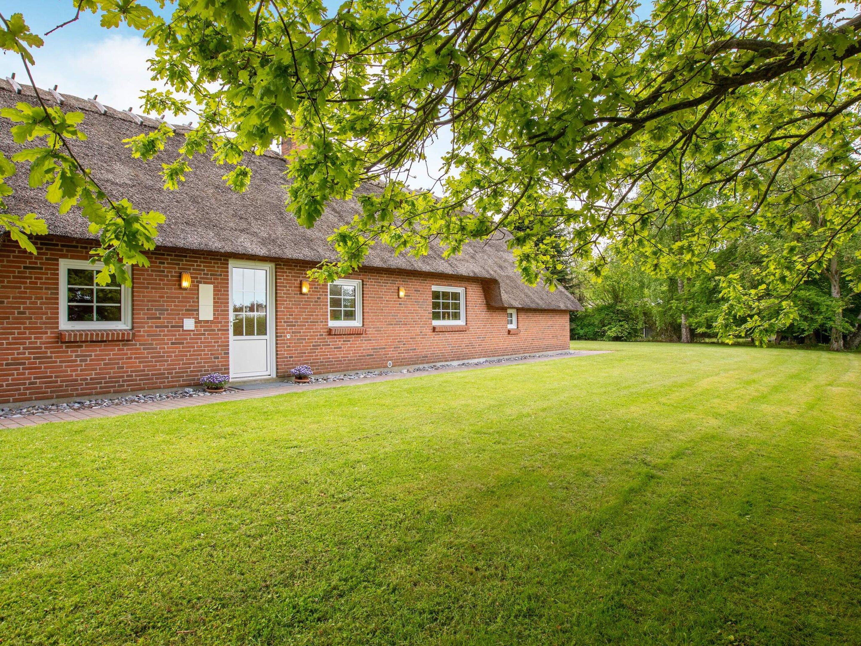 A brick house with a thatched roof, a well-maintained lawn, and a clear sky.