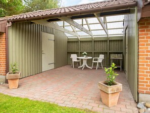 A covered outdoor area with a brick floor, two white chairs, a small table, and two potted plants. - Holiday Home in VÃ¦ggerlÃ¸se (Vaeggerlose)