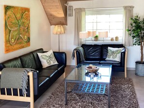 A living room with a glass coffee table, two sofas with butterfly pillows, a painting on the wall, and a potted plant. - Holiday Home in VÃ¦ggerlÃ¸se (Vaeggerlose)