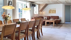 Una sala de estar moderna con comedor, que presenta mobiliario de madera, una escalera y un ventanal grande.