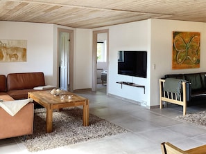 Een woonkamer met een houten plafond, een aan de muur bevestigde televisie, een bank, een salontafel en een vloerkleed.