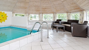 Una piscina interior con suelo de baldosas y techo de madera. Se observan sillas de mimbre y una decoración con motivos de sol en la pared.