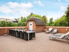 An outdoor patio with a brick wall, a thatched-roof structure, and a table with chairs. - Holiday Home in VÃ¦ggerlÃ¸se (Vaeggerlose)