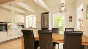 A modern kitchen with white cabinets, stainless steel appliances, and a dining area with a wooden table and leather chairs. - Holiday Home in LÃ¦sÃ¸ (Læsø)
