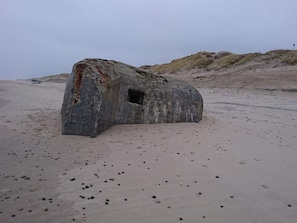 A large, weathered rock formation with a small opening, surrounded by a sandy beach. - Holiday Home in RingkÃ¸bing (Ringkobing)