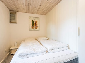 A hotel room with a wooden ceiling, a bed with white bedding, a nightstand with a lamp, and a framed picture on the wall.