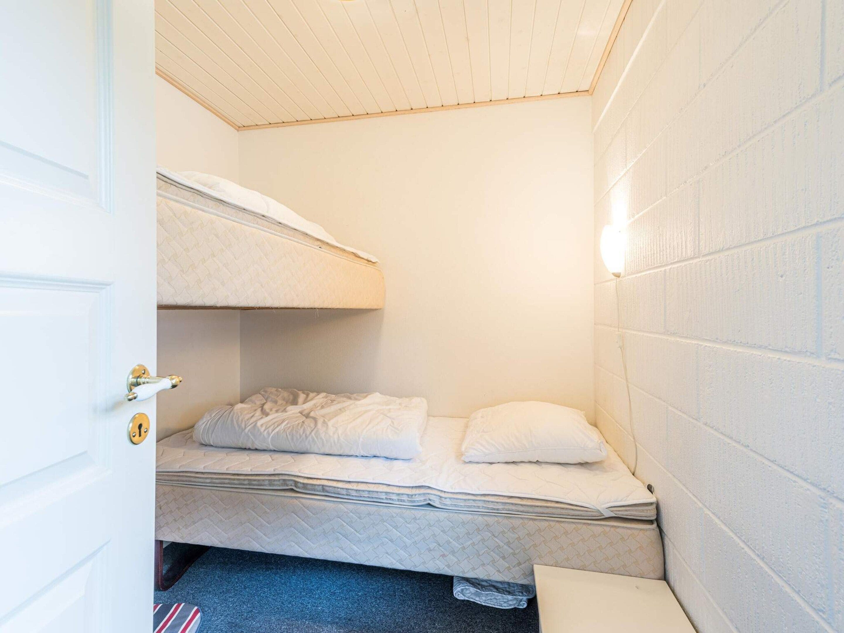A small, compact room with a bunk bed, a single bed, a door with a keyhole, and a wall-mounted light fixture.