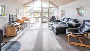 Ein geräumiges Wohnzimmer mit hoher Decke, großen Fenstern und einem modernen Kronleuchter.