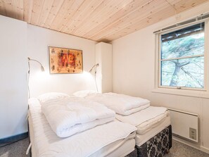 Une chambre à coucher avec un lit, un tableau, une fenêtre donnant sur des arbres et un radiateur.