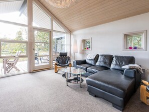 Un salon spacieux doté d’une grande porte vitrée donnant sur un espace extérieur, d’un canapé en cuir noir, d’une table basse en verre et d’un plancher en bois.