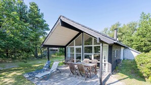 Ein Haus mit überdachter Terrasse, Essbereich und großem Fenster mit Blick auf ein bewaldetes Gelände.