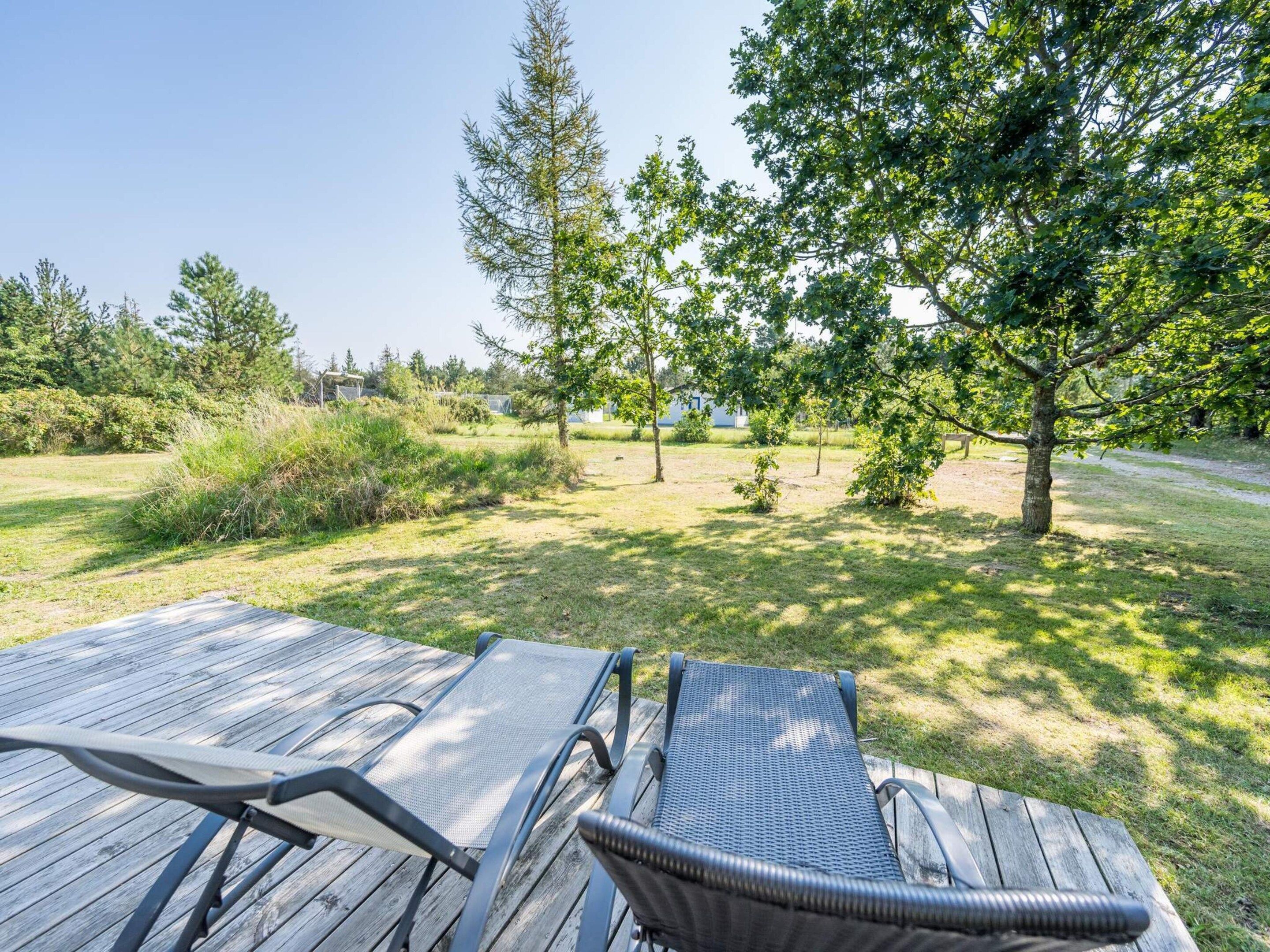 A wooden deck with two lounge chairs facing a grassy area with trees.