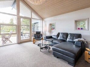 A modern living room with a glass door leading to an outdoor area, a leather sofa, a glass coffee table, and a wooden floor. - 4 Star Holiday Home in Norre Nebel (Norre Nebel)
