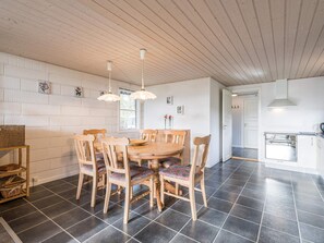 A dining area with a round wooden table and chairs, a hanging light fixture, and a white brick wall with decorative tiles. - 4 Star Holiday Home in Norre Nebel (Norre Nebel)