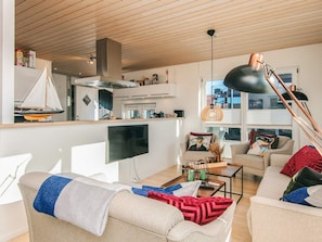 A modern living room with a flat-screen TV, a sofa with a throw blanket, a coffee table, and a dining area with a sailboat model.