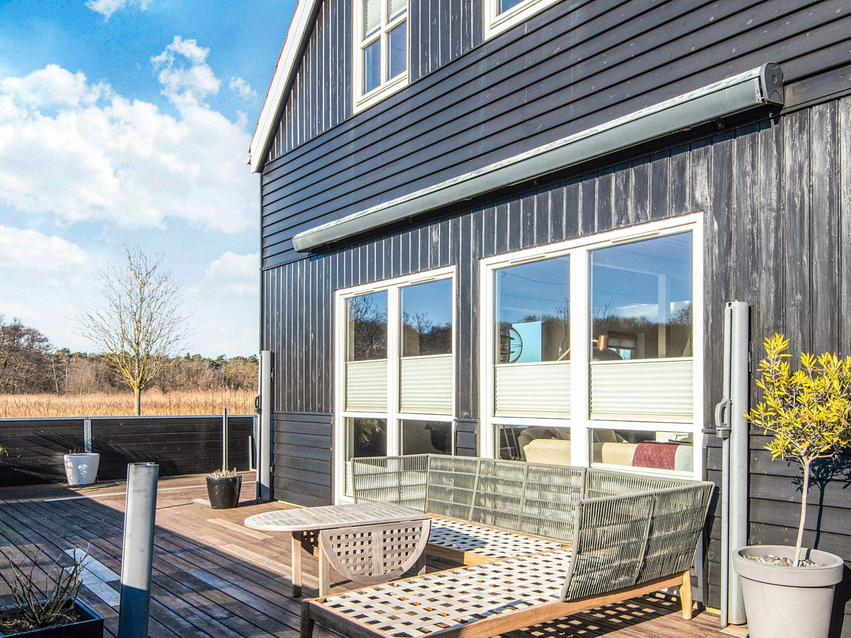 Une maison moderne avec une terrasse, un canapé et des plantes en pot.