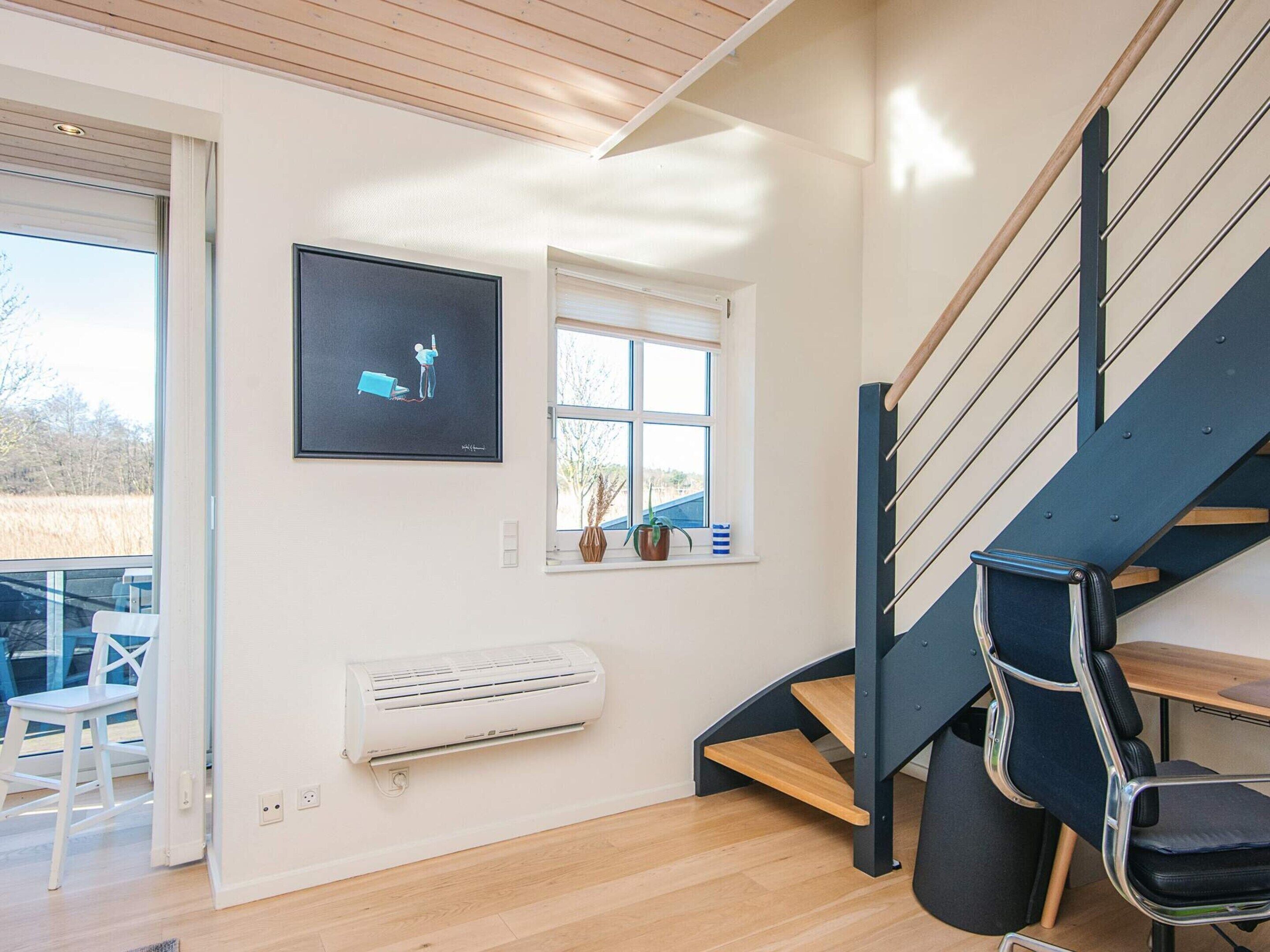 A modern interior with a staircase, a mounted air conditioner, a framed artwork, and a window with a view of the outdoors.