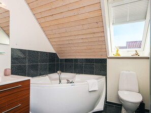 A modern bathroom with a freestanding bathtub, a toilet, a vanity with drawers, and a window with a view of buildings. - Holiday Home in Juelsminde (Juelsminde)