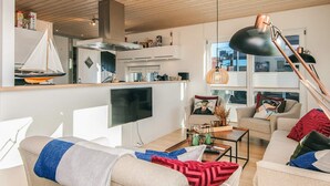Una sala de estar moderna con un televisor grande, asientos cómodos, una zona de cocina y vistas al exterior.