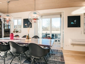 A modern dining area with a large table, black chairs, and a glass-top table. - Holiday Home in Juelsminde (Juelsminde)