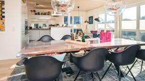 Una cocina moderna con armarios blancos, encimera de madera y un comedor con mesa de vidrio y sillas negras.