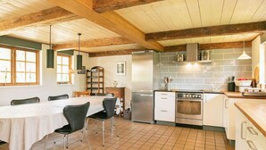 A kitchen with wooden beams, a tiled floor, a dining table with chairs, and a refrigerator. - Idyllic Countryside Retreat-by Traum (Rudkobing)