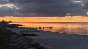 Uma praia com costa rochosa, mar calmo e pôr do sol.