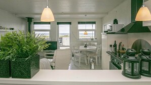 Cozinha com área de refeições, janelas amplas e vista para o mar.
