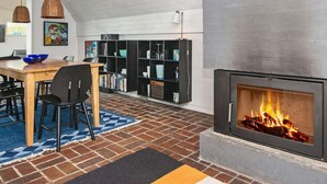 Uma sala de estar acolhedora com lareira, uma mesa de jantar e uma estante de livros.