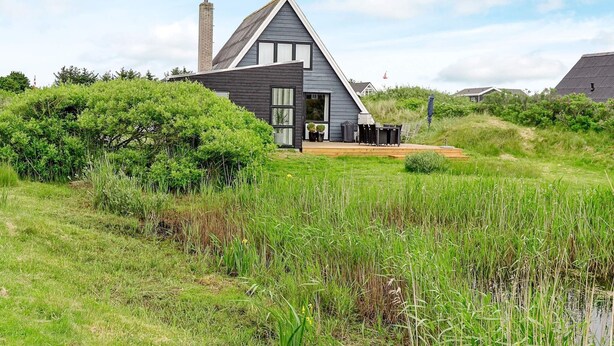 Uma casa moderna com telhado inclinado, chaminé e um deck com mobiliário de exterior.