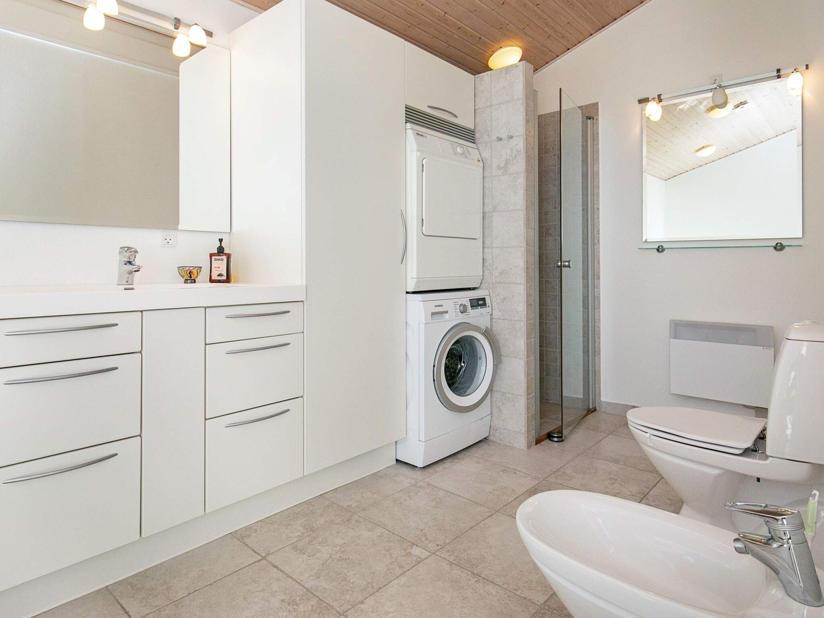 A modern bathroom with a built-in washing machine, a toilet, and a large mirror.