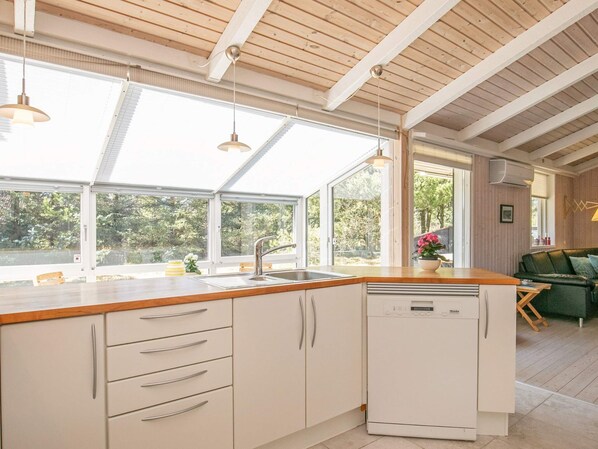 A modern kitchen with a wooden countertop, white cabinets, a built-in dishwasher, and large windows offering a view of the outdoors. - Holiday Home in Strandby (Strandby)